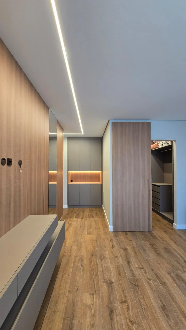 Corredor de closet com armários dos dois lados, bancada suspensa e iluminação linear correndo no forro