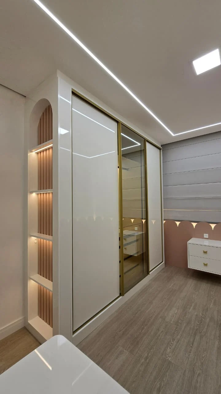 Quarto infantil com guarda-roupa de portas de correr em laca e vidro com perfil dourado, nicho arqueado iluminado e cômoda suspensa