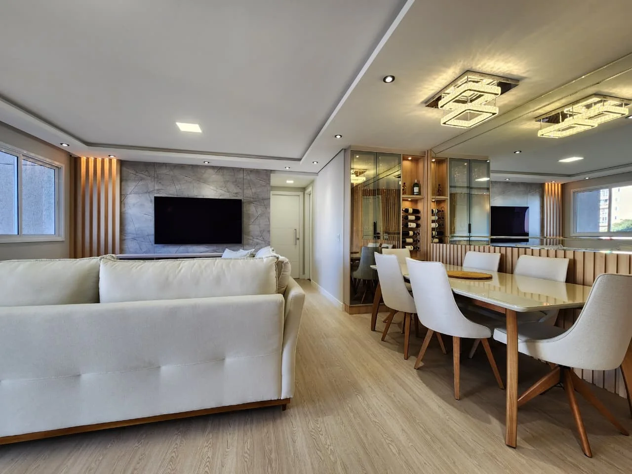 Living e sala de jantar integrados, com painel de TV em porcelanato marmorizado, adega em vidro e boiserie ripada, executados pela Castani em Curitiba