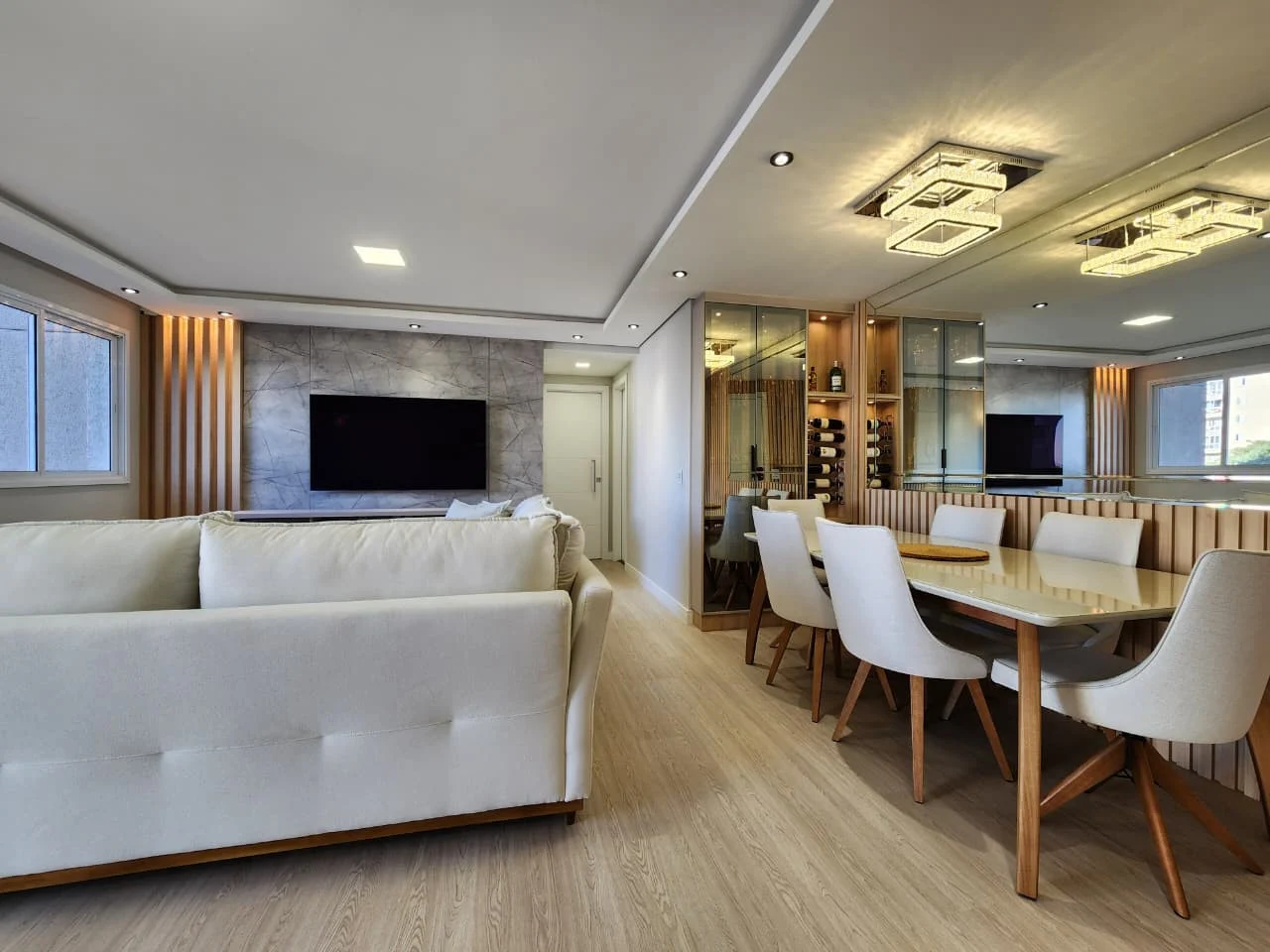 Living e sala de jantar integrados, com painel de TV em porcelanato marmorizado, adega climatizada em vidro e boiserie ripada atrás da mesa